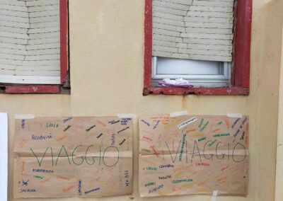 Due cartelloni con la parola "viaggio" e tante parole colorate scritte a mano, appesi a un muro