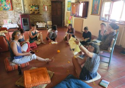 Gruppo di donne sedute in cerchio cuce e lavora con stoffe e filo in una sala accogliente piena di quadri