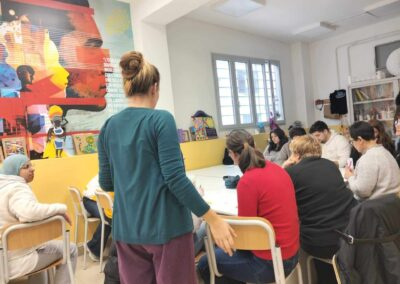 Conduttrice in piedi accompagna un gruppo seduto attorno a un tavolo in uno spazio educativo durante un laboratorio