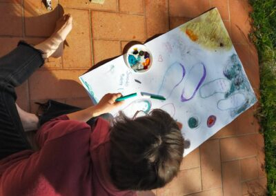 Vista dall'alto di una donna che disegna a pastello su un grande foglio all'aperto, tra colori e parole scritte