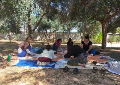 Gruppo di donne sedute a terra su teli disegna e crea insieme all'ombra degli ulivi durante un laboratorio all'aperto