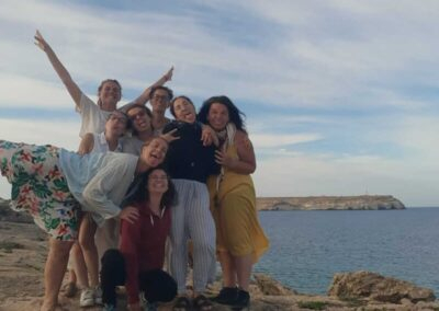 Gruppo di donne ride e posa allegramente su una scogliera affacciata sul mare durante un ritiro a Lampedusa