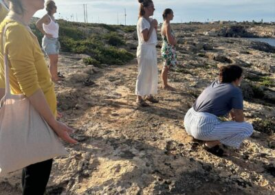 Gruppo di donne in piedi su una costa rocciosa guarda l'orizzonte nella luce calda del tramonto durante un ritiro