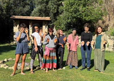 Gruppo di donne sorridenti in giardino mostra le mani dipinte di arancione durante un laboratorio esperienziale