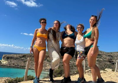 Cinque donne sorridenti e abbracciate su una scogliera affacciata sul mare turchese durante un ritiro a Lampedusa