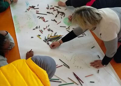 Vista dall'alto di un gruppo di persone che disegna insieme su un lungo cartellone a terra con tanti pastelli