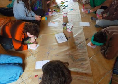 Gruppo di donne sedute a terra disegna e scrive su un lungo cartellone con la frase "insieme uomini e donne in cerchio