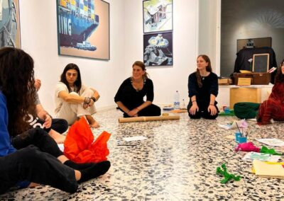 Gruppo di donne sedute in cerchio sul pavimento di una galleria d'arte durante un laboratorio creativo