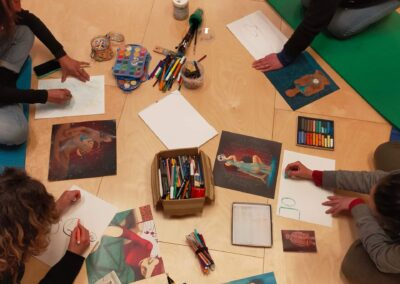Vista dall'alto di donne sedute in cerchio che disegnano con colori e immagini durante un laboratorio creativo