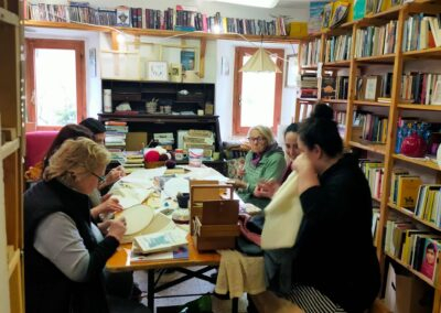 Gruppo di donne riunite attorno a un tavolo che ricamano in una stanza accogliente piena di libri