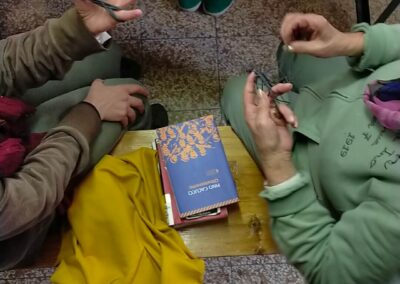 Vista dall'alto di due donne sedute che ricamano con telaio, fili e libri, durante un laboratorio meditativo