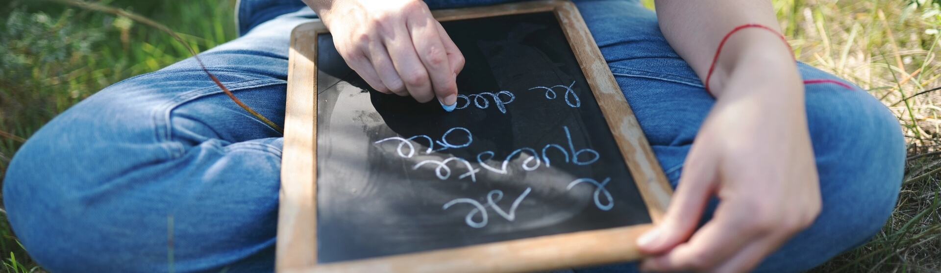 Mani che scrivono col gesso su una lavagnetta seduti nell'erba, gesto di riflessione e scrittura di sé