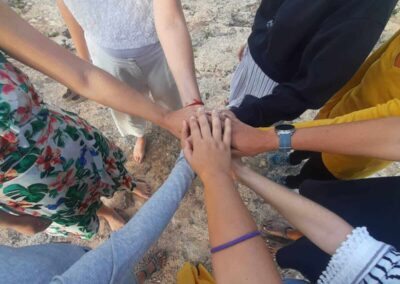Mani di un gruppo di donne unite al centro di un cerchio su una scogliera affacciata sul mare durante un ritiro