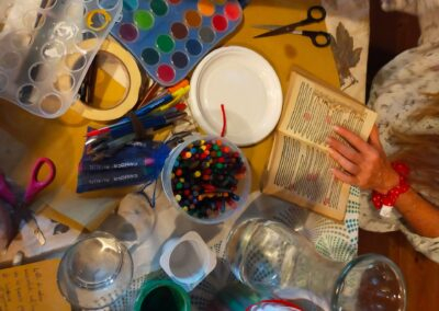 Tavolo con acquerelli, pastelli a cera, forbici e un libro tra le mani durante un laboratorio creativo