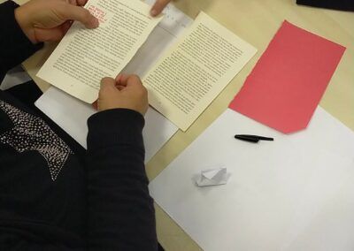 Mani di partecipanti che sfogliano pagine e condividono letture attorno a un tavolo durante un laboratorio